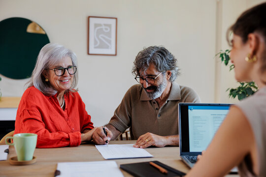 Senior couple smiling and signing contract with financial advisor