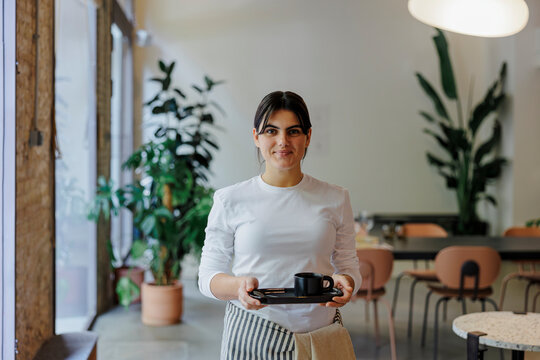 Waitress holding tray with cup of coffee in restaurant
