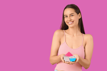 Young woman with condoms and contraceptive pills on purple background