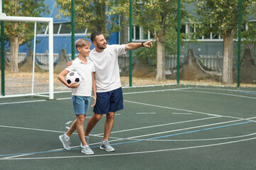 Father and his son with ball on soccer pitch