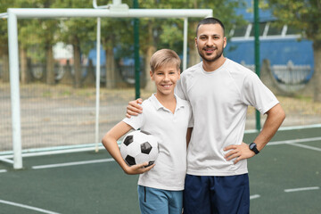 Father and his son with ball on soccer pitch