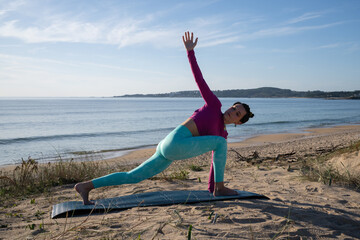 Yoga instructor performing extended side angle pose on beach mat