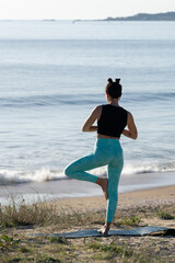 Young woman practicing yoga tree pose on the beach at sunrise