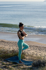 Yoga instructor practicing tree pose on the beach on a sunny day