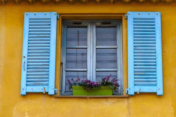 Mediteranes Fenster mit blauen Holzfensterläden und einem Blumenkasten mit Lavendel vor einer gelben Fassade