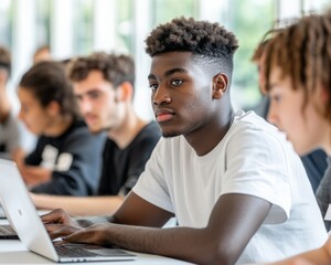 Focused African American male student sits at a table, engaged in a classroom setting using a laptop.