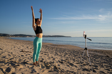 Yoga instructor streaming online class on the beach at sunrise