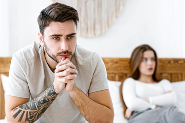 Impotence concept. Sad man presses hands to his chin and ponders, wife disappointed folded arms at...