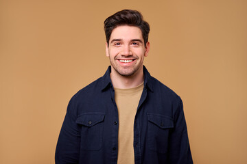 A portrait of a smiling young man set against a soft beige background, showcasing joy and warmth
