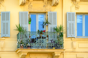 Fensterfassade mit Fensterläden und Pflanzen an einem Balkonfenster in Nizza, Frankreich 