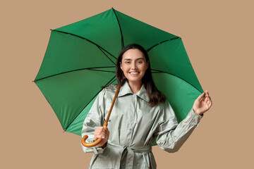 Happy young woman with umbrella on beige background