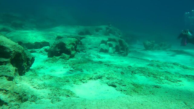 Deep seabed with rock and scuba divers explorers. Underwater video from scuba diving in the ocean, rocks and stones underwater. Sand and stones, travel footage from scuba diving trip.