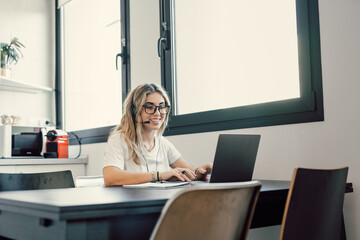 Happy millennial female in headphones watch webinar on laptop in modern office, smiling young businesswoman have fun laugh talk on video call with client or colleague use wireless Internet connection.