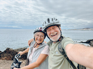 Two happy old mature people enjoying and riding bikes together to be fit and healthy outdoors. Active seniors having fun taking a selfie picture with camera