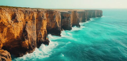 Golden cliffs meeting turquoise waters, viewed from a high perspective, with waves crashing at the...