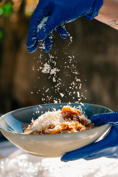 Chef garnishing pasta with grated cheese using blue gloves