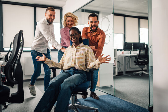 Office workers pushing colleague sitting on chair