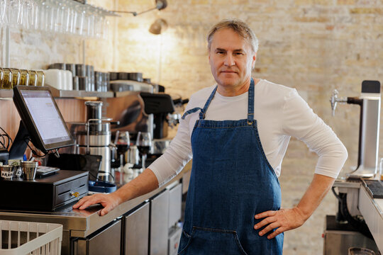 Confident barista posing behind counter in coffee shop