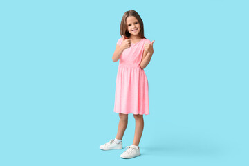 Portrait of happy little girl showing thumbs-up on blue background