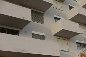 There exists a large building characterized by its numerous windows and a variety of balconies,...