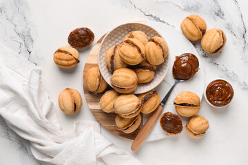 Bowl and cutting board of sweet walnut shaped cookies with boiled condensed milk on white background