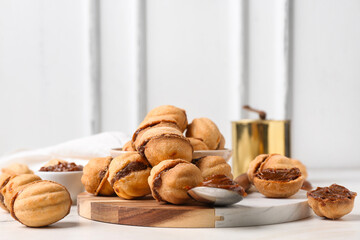 Bowl and cutting board of sweet walnut shaped cookies with boiled condensed milk on white background