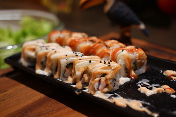 Sushi roll with salmon, avocado, cheese and sauce on black plate