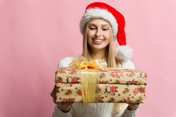 Smiling woman in Christmas hat with wrapped gifts in front of pink background.