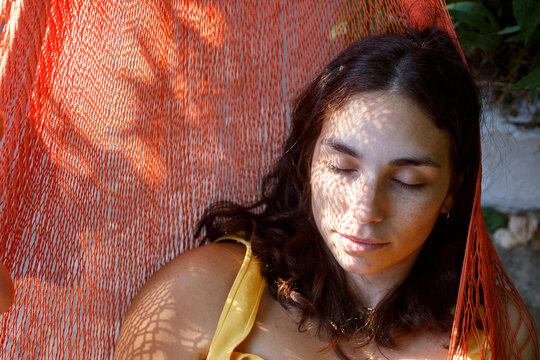 Woman lying on hammock in sunlight with eyes closed