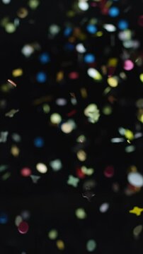 Vertical video of Colorful and multiform glitter confetti explosion on a black background, studio shot. Moment of happiness and festivity concept.