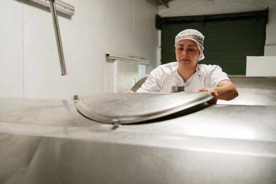 Cheese factory worker opening milk tank in food production facility