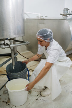 Dairy employee filling buckets with milk from pasteurizer