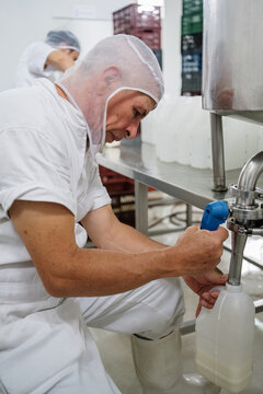 Focused dairy factory worker filling yogurt bottle from tank