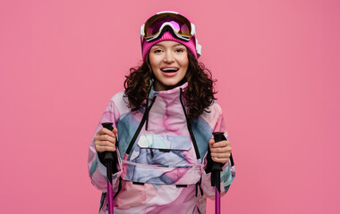 attractive smiling woman posing on pink background with skis in snow winter skiing sport suit