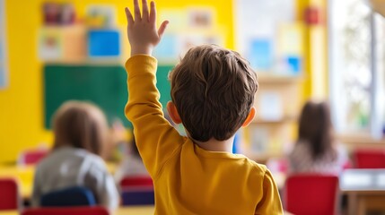 A young boy raises his hand in a classroom, eager to answer a question.