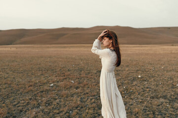 Lonely woman in white dress standing in open field with hands on head, beauty and solitude in nature