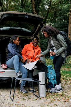Friends looking at map while planning road trip in autumn forest