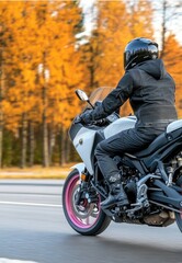 Fototapeta premium A young man in a black helmet and jacket rides a white and pink sport bike with red wheels on an empty parking
