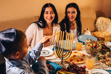 Little boy lighting a golden menorah at Hanukkah.