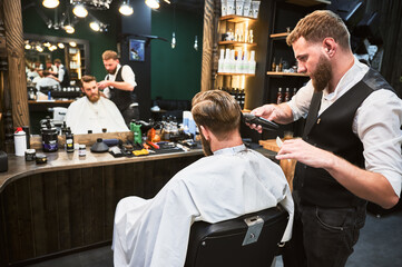 Professional barber using comb and electric shaver to cut side hair. Close-up view of male customer getting stylish haircut.