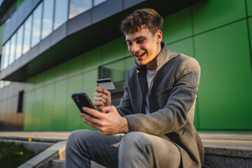 young man sit on staircase shop online on cellphone with credit card