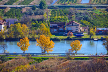 Autumn landscape with vibrant trees along the river and rural houses surrounded by lush greenery.