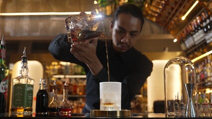 Asian bartender pouring mixed cocktail whiskey into cool glass textured cooling ice drink making special advertisement creative focusing alcohol refresh showcase at luxurious warm light pub. Vinosity.
