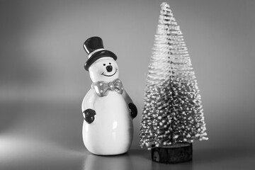 Festive New Year decoration, decor of a ceramic snowman with a red hat and a bow on a gray...