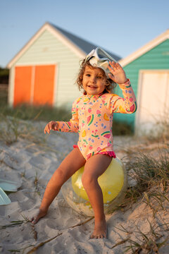 A toddler sitting on a ballon at the beach with googles.