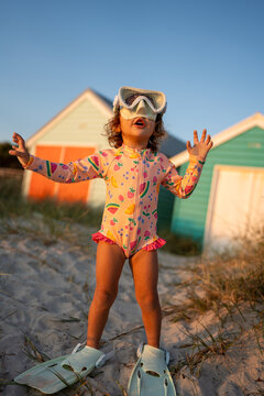 A toddler standing at the beach with googles and fins.