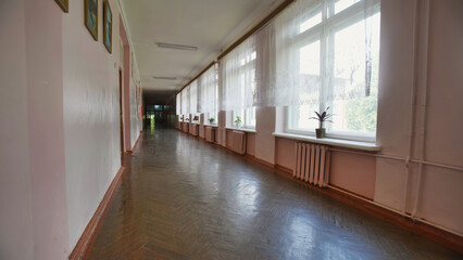 Polished wooden floor reflecting sunlight in an empty school corridor with plants on windowsills on...