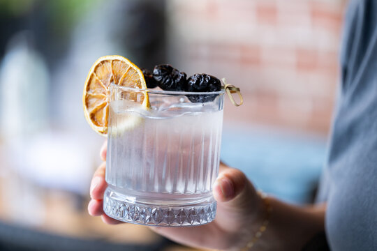 Woman holding plum vodka cocktail outdoors