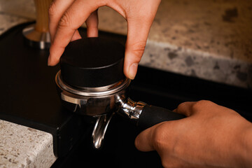 A professional barista. Concept of modern warm coffee shop and Preparing process of coffee. Close up of a hand holding a filter holder with ground coffee in a Cafe or coffee shop.