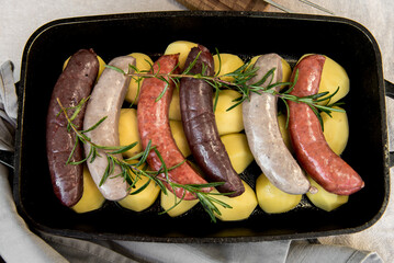 Close-up of bowl with raw homemade blood sausage, pork sausage and chorizo in oven with potatoes....